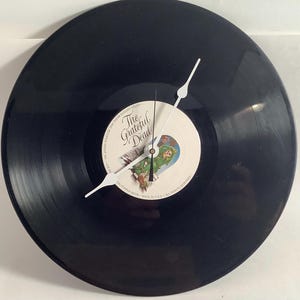 May include: A black vinyl record clock with white clock hands. The center label features the text "The Grateful Dead" and a colorful illustration. The clock is a unique decorative item.