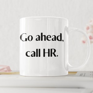 Puede incluir: Taza de café de cerámica blanca con texto negro que dice "Go ahead, call HR."