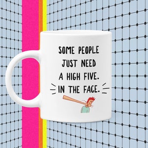 May include: White ceramic mug with a black and white illustration of a person getting hit in the face with a baseball bat. The text on the mug reads "Some people just need a high five. In the face."