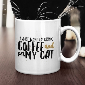 Może przedstawiać: Biały ceramiczny kubek do kawy z czarnym tekstem, który brzmi "Chcę tylko pić kawę i głaskać mojego kota". Czarno-biały kot pije z kubka.