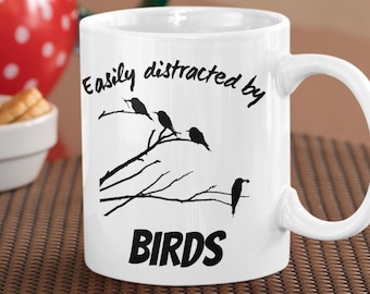May include: White ceramic mug with black text that reads "Easily distracted by BIRDS" and a silhouette of birds on a branch.