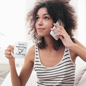 May include: White ceramic mug with black text that reads "If you're happy and you know it it's your meds" with a graphic of two pills. A woman is holding the mug and talking on a white cell phone.