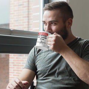 May include: White ceramic mug with a red warning sign that reads "WARNING MAY SPONTANEOUSLY START TALKING ABOUT AIRPLANES". A small airplane icon is in the center of the sign. A person is holding the mug and drinking from it.