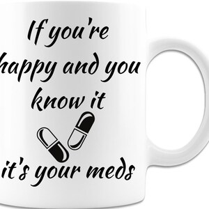 May include: White ceramic mug with black text that reads "If you're happy and you know it, it's your meds." Two black and white pills are illustrated below the text.
