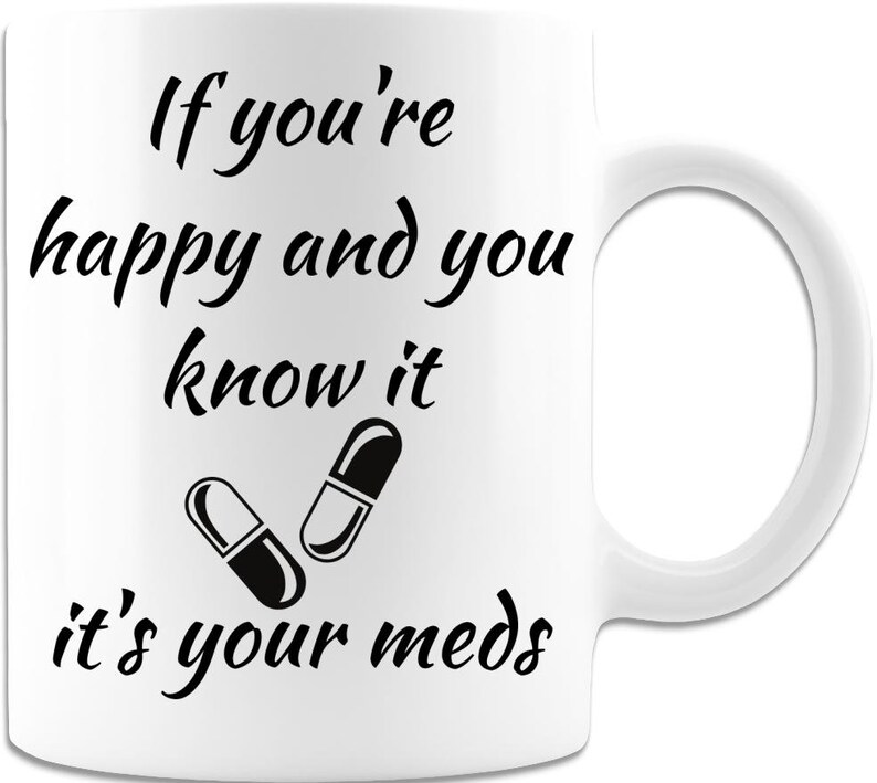 May include: White ceramic mug with black text that reads "If you're happy and you know it, it's your meds." Two black and white pills are illustrated below the text.