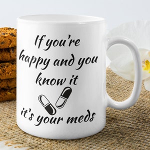 May include: White ceramic mug with black text that reads "If you're happy and you know it, it's your meds." Two black and white pills are pictured below the text.