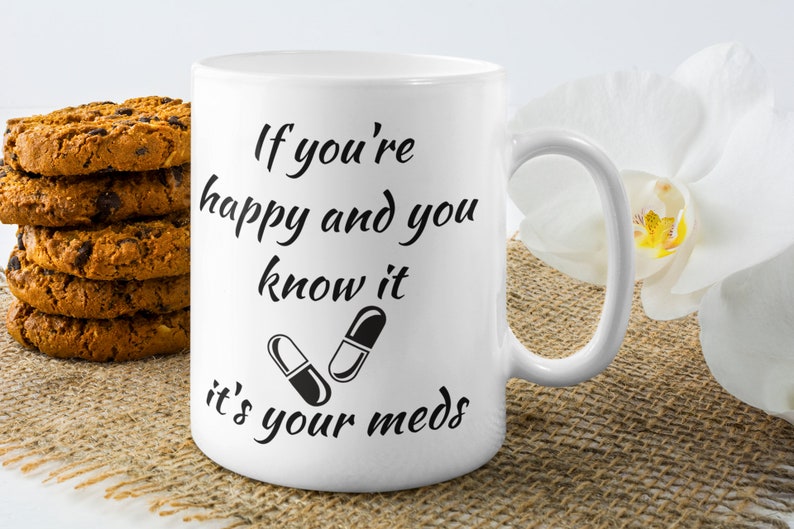 May include: White ceramic mug with black text that reads "If you're happy and you know it, it's your meds." Two black and white pills are pictured below the text.