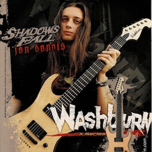 Peut inclure: Un musicien aux longs cheveux bruns joue d'une guitare électrique Washburn X Series. La guitare est en bois naturel avec des accastillages noirs. Le musicien porte une chemise noire. L'image comprend le texte "SHADOWS FALL" et "Washburn X Series".