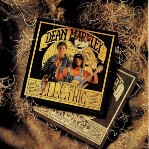 Könnte beinhalten: Ein schwarzes und weißes Albumcover mit dem Text "DEAN MARLEY ELECTRIC" und einem Bild von zwei Männern, die Gitarre spielen. Das Albumcover befindet sich auf einem braunen Jutesack-Hintergrund.