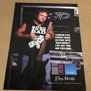 Op de afbeelding: Een zwart-witfoto van een muzikant die een Dean Markley gitaar vasthoudt. De muzikant draagt een zwart T-shirt met de tekst "Born to be Bad" erop. De tekst "I demand a big punchy sound on stage with Dean Markley. I get just that, and then some." is afgedrukt op de afbeelding. De muzikant houdt een Dean Markley gitaar vast en de tekst "Dean Markley" is afgedrukt onderaan de afbeelding.