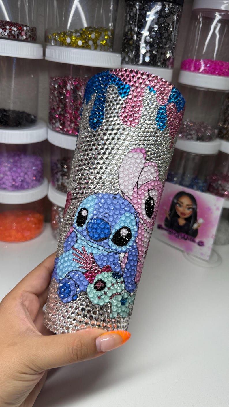 Puede incluir: Un vaso adornado con pedrer&iacute;a con los personajes Stitch y Angel de Lilo & Stitch. El vaso est&aacute; cubierto de pedrer&iacute;a plateada con detalles azules y rosas. Los personajes est&aacute;n representados con pedrer&iacute;a de colores.