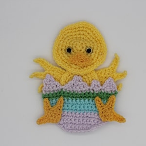 May include: A handmade crochet chick emerging from a colorful egg. The chick is yellow with a peach beak and black eyes. The eggshell is lavender, green, and blue. This Easter-themed item is perfect for spring decor.