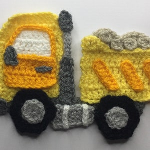 May include: A handmade crochet dump truck in yellow, gray, black, and red. The truck features a yellow cab with a white window, black wheels, and a gray exhaust pipe. The truck bed is also yellow with three orange accents.