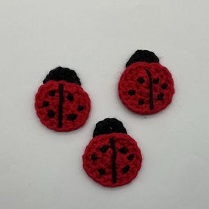 May include: Three handmade crochet ladybug appliques. Each ladybug is red with black spots and a black head. The appliques are round and appear to be made of yarn.