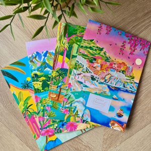 Peut inclure: Plusieurs carnets colorés avec des illustrations de paysages vibrants. Les carnets présentent des scènes de montagnes, de plantes tropicales et de villes côtières. Un carnet porte le texte "Notes Manarola". Les carnets sont disposés sur une surface en bois.