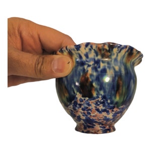 May include: A small, blue and white ceramic pot with a ruffled rim. The pot has a mottled glaze with brown, green, and pink accents.