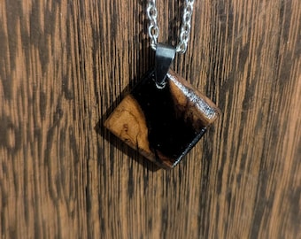 May include: A diamond-shaped pendant necklace with a wood and black resin inlay. The pendant is attached to a silver chain.