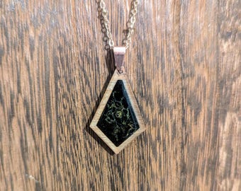 May include: A gold chain necklace with a black and gold diamond-shaped pendant. The pendant has a black resin inlay with gold flecks.