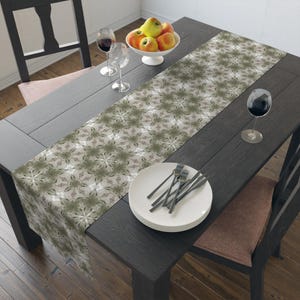 May include: A brown and white table runner with a geometric pattern. The runner is on a dark wood table with a bowl of apples, two wine glasses, and a stack of white plates with silverware.