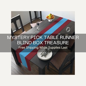 May include: A long rectangular table runner featuring a bold color-blocked design with a wide central light blue stripe flanked by two deep maroon side panels. The text MYSTERY PICK TABLE RUNNER BLIND BOX TREASURE is printed across the center.
