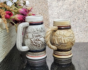 May include: Two ceramic beer steins with intricate designs. One stein features a vintage car with the text "1910 Stanley Steamer" and the other stein features a sailing ship scene with the text "Dub-Headed"