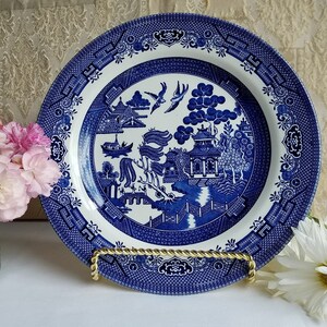 Puede incluir: Plato de porcelana azul y blanco con un diseño tradicional de sauce. El plato presenta un paisaje estilizado con un puente, una pagoda y un sauce.