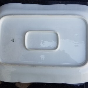 Puede incluir: Plato de servir de porcelana blanca con una secci&oacute;n central elevada y bordes festoneados. El plato tiene una marca del fabricante en la parte inferior que dice "H.F.C.H."