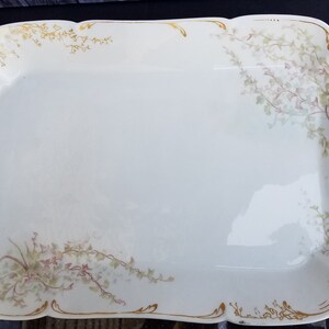 Puede incluir: Una fuente de servir de porcelana blanca con ribete dorado y dise&ntilde;o floral. La fuente tiene dos asas a los lados.