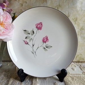 May include: White ceramic dinner plate with a black rim and a delicate design of pink roses and gray leaves.