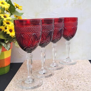 May include: Set of four red wine glasses with a clear stem and base. The glasses have a cut glass design.
