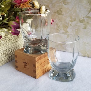 May include: Two clear glass tumblers with a rounded, flared base. The tumblers are sitting on a wooden box with Japanese characters.