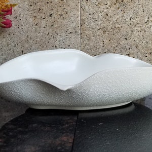 Puede incluir: Tazón de cerámica blanco con una superficie texturizada y una forma ondulada orgánica.