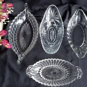 Puede incluir: Cuatro platos de servir de vidrio transparente con diferentes patrones. Los platos son de forma ovalada y tienen un borde elevado. Todos están sobre un fondo de tela negra.