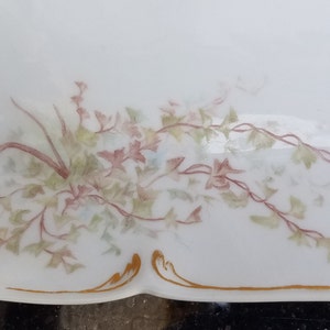 Puede incluir: Un plato de servir de porcelana blanca con un borde dorado y un delicado dise&ntilde;o floral en tonos de rosa y verde.