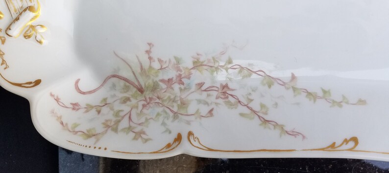 Puede incluir: Un plato de servir de porcelana blanca con un borde dorado y un delicado dise&ntilde;o floral en tonos de rosa y verde.