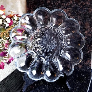 May include: Clear glass serving dish with a scalloped edge and a central starburst design. The dish has multiple compartments, perfect for serving appetizers or snacks. The glass is transparent, allowing the contents to be visible.