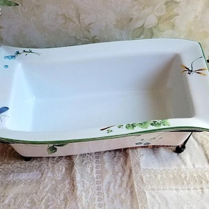 May include: Rectangular white ceramic serving dish with black metal handles. The dish is decorated with blue butterflies, green leaves, and a dragonfly. The dish sits on a black metal stand.