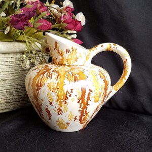 May include: A white ceramic pitcher with a brown and yellow marbled design. The pitcher has a wide mouth and a handle.