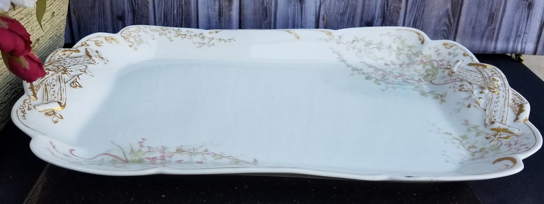 Puede incluir: Una bandeja rectangular blanca para servir con borde festoneado y dise&ntilde;os florales dorados y rosados.