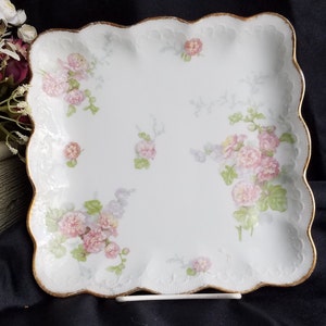 May include: A white porcelain serving tray with a scalloped edge and a gold trim. The tray is decorated with a floral pattern of pink and purple flowers.