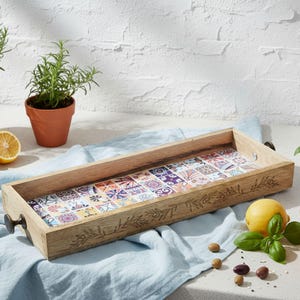 Könnte beinhalten: Rechteckiges Serviertablett aus Holz mit farbenfrohem Fliesenmuster im Inneren. Das Tablett hat Metallgriffe und ist mit geschnitzten floralen Mustern verziert. Das Bild zeigt auch Kräuter in Töpfen, Zitronen und Oliven.