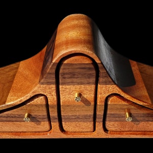 May include: A wooden box with three drawers and a curved top. The box is made of different types of wood, including walnut and mahogany. The drawers have brass knobs.