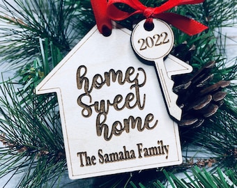 May include: A wooden house-shaped ornament with the text "home sweet home" and "The Samaha Family". A small wooden key with the year "2022" is attached to the ornament.