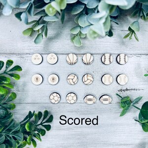Pode incluir: Um conjunto de 18 fichas redondas de madeira com diferentes designs de bolas de desporto, incluindo basquetebol, beisebol, futebol, voleibol e bowling. As fichas est&atilde;o dispostas em tr&ecirc;s filas de seis sobre uma superf&iacute;cie de madeira clara. A palavra "Scored" est&aacute; impressa abaixo das fichas.