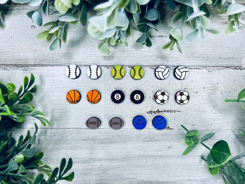 Pode incluir: Um conjunto de 12 brincos de madeira em forma de bola de esporte. Os brincos s&atilde;o pintados em v&aacute;rias cores, incluindo laranja, amarelo, azul, branco e preto. As bolas de esporte incluem beisebol, basquete, futebol, t&ecirc;nis, v&ocirc;lei e boliche.