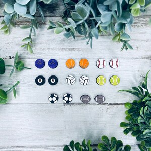Pode incluir: Um conjunto de 12 pares de brincos com tema esportivo. Os brincos s&atilde;o feitos de madeira e apresentam v&aacute;rios esportes, como beisebol, basquete, futebol americano, futebol, v&ocirc;lei e boliche. Os brincos s&atilde;o pintados em v&aacute;rias cores, incluindo vermelho, branco, azul, verde, amarelo, laranja e preto.
