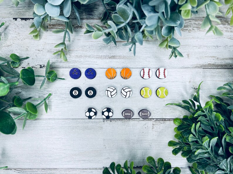 Pode incluir: Um conjunto de 12 pares de brincos com tema esportivo. Os brincos s&atilde;o feitos de madeira e apresentam v&aacute;rios esportes, como beisebol, basquete, futebol americano, futebol, v&ocirc;lei e boliche. Os brincos s&atilde;o pintados em v&aacute;rias cores, incluindo vermelho, branco, azul, verde, amarelo, laranja e preto.