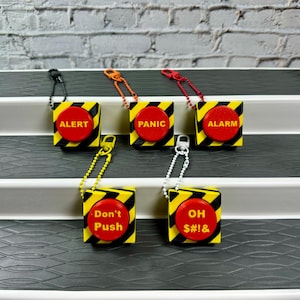 May include: Four yellow and black button keychains with red buttons. The buttons have the words "Alert", "Panic", "Alarm", "Don't Push", and "Oh S#!&" on them.