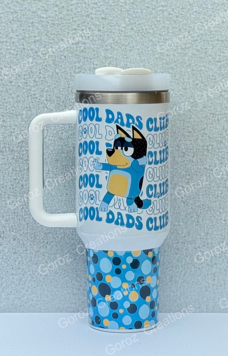 May include: A white stainless steel travel mug with a blue and yellow cartoon dog design. The mug has a white handle and lid. The text "Cool Dads Club" is printed on the mug.