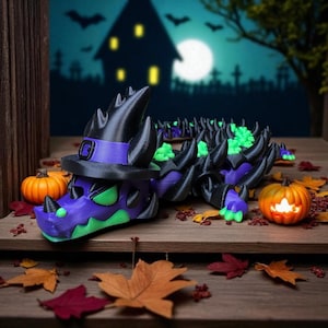 May include: A Halloween-themed, articulated dragon figurine in purple, black, and green, wearing a witch's hat. The dragon is surrounded by pumpkins and autumn leaves, with a spooky haunted house backdrop.